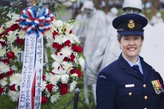 A woman in uniform stands next to a memorial of flowers