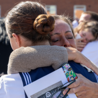 Two women hug, one wearing a navy uniform
