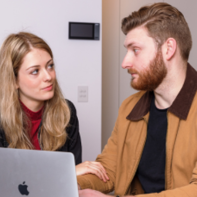 A woman and man sit in front of a laptop